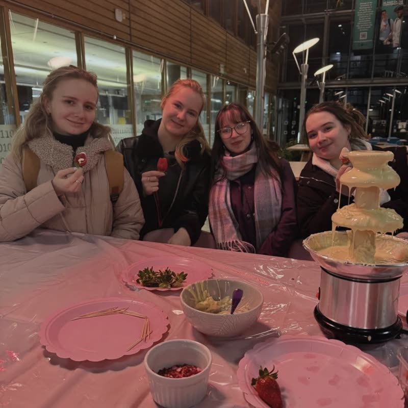 Four members holding chocolate covered strawberries next to a white chocolate fountain.