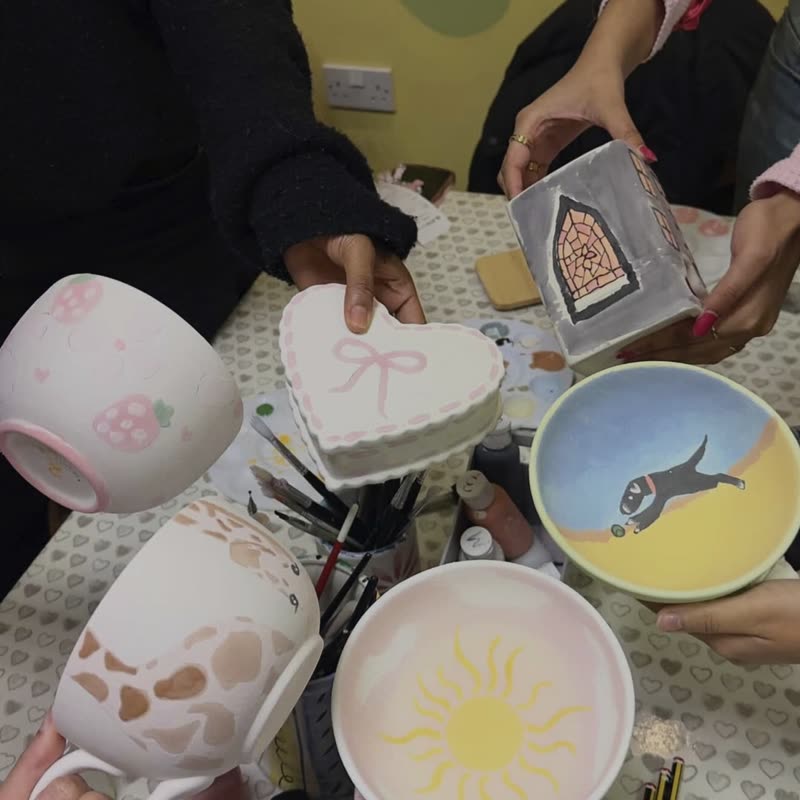 The finished pottery held up together: a heart box with a bow, a strawberry mug, a sun bowl and a bowl with a dog on it.
