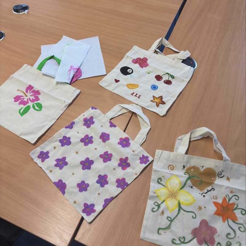 Four painted tote bags laid out on a table, with flowers, cherries and hearts on them.